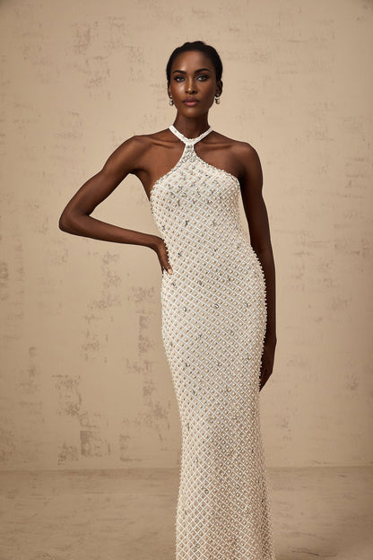 Woman wearing long white halterneck maxi dress with embellished details standing against plain background