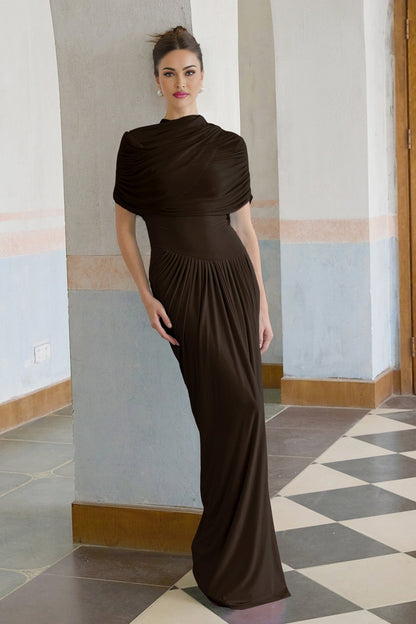 Woman wearing long brown asymmetric pleated maxi dress with flowing skirt and one shoulder design