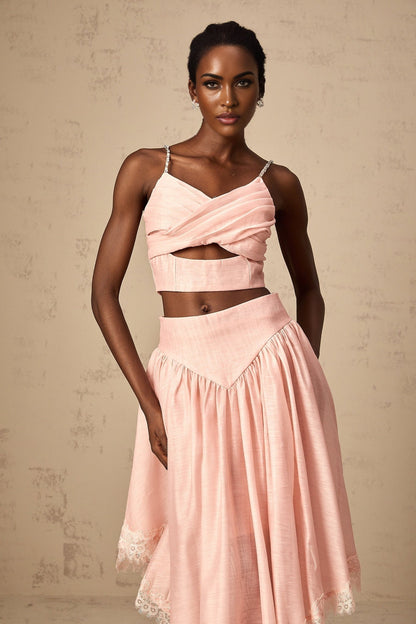 Woman wearing a pink two piece outfit consisting of an asymmetric ruffled top and matching skirt