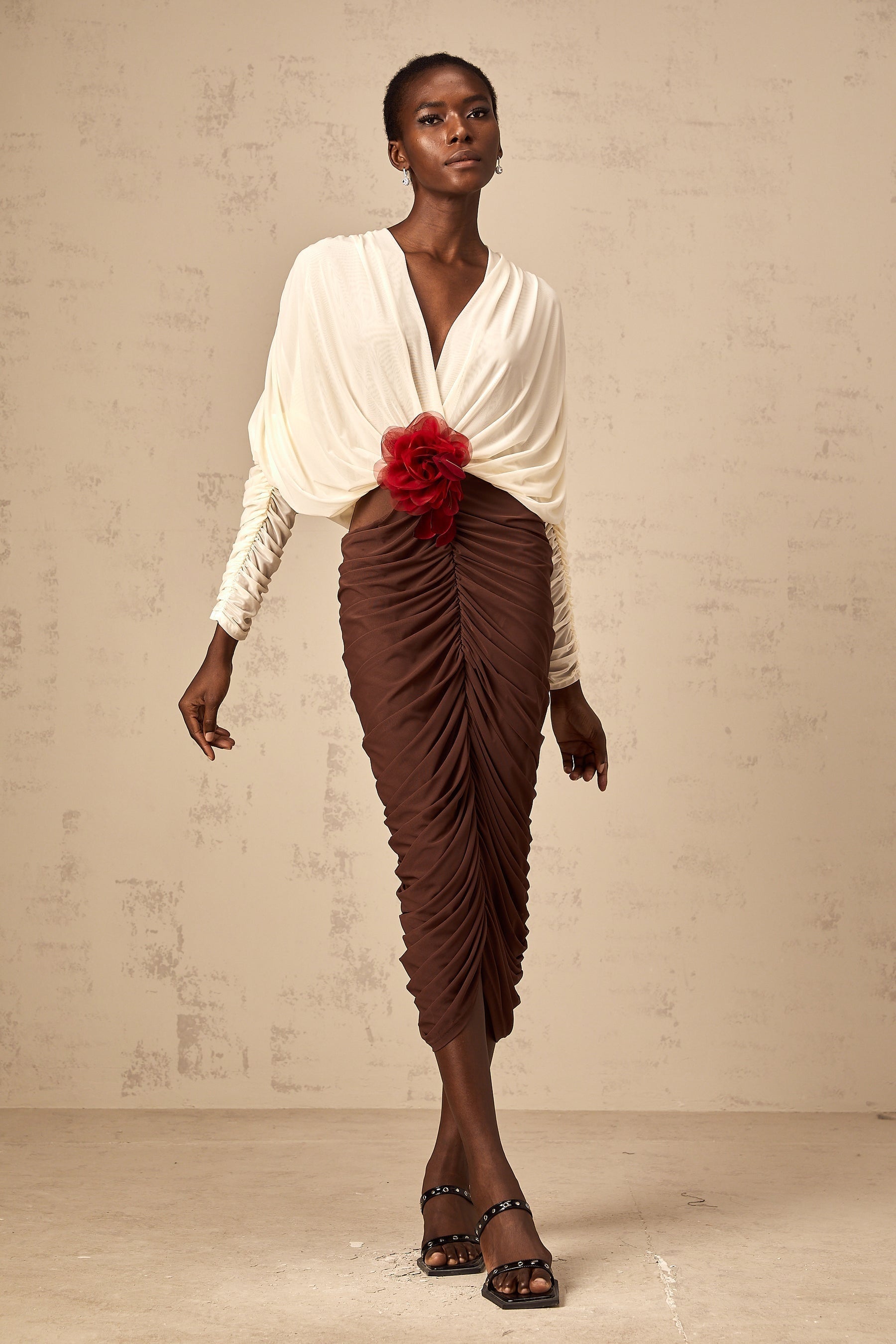 A midi dress with color blocking and ruching featuring a flower brooch The dress is named Leontine and has a mid length design