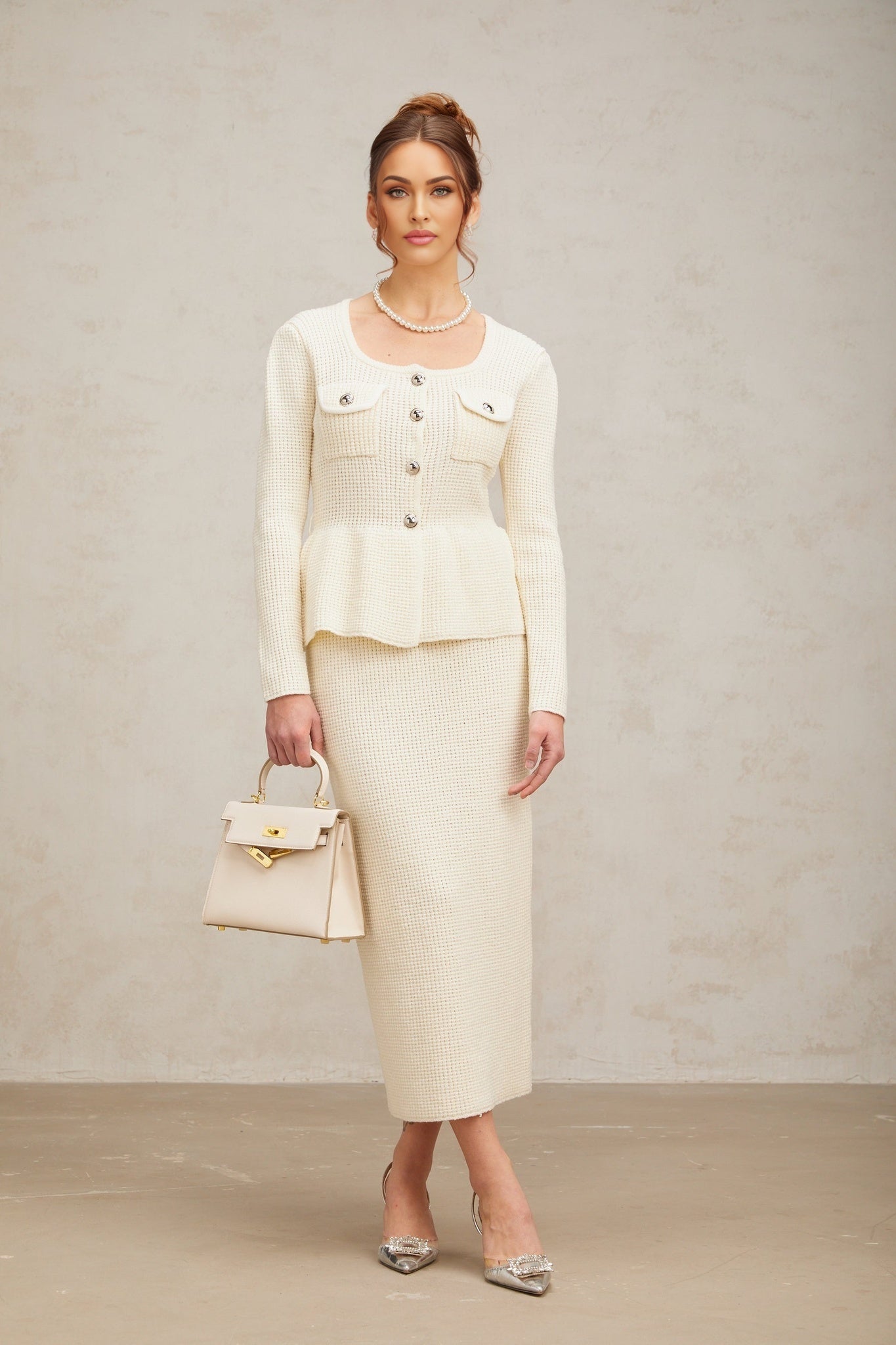 Woman wearing white knitted crop top and matching midi skirt standing against plain background