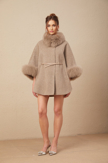 A woman wearing a brown wool cape coat with fur trim and a belt cinching the waist