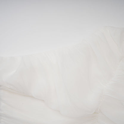 A woman wearing a white matching set consisting of a creased top and trousers standing against a plain background