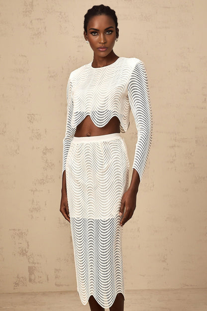 Young woman wearing a white twopiece outfit consisting of a wavy woven top and matching skirt standing against a plain background