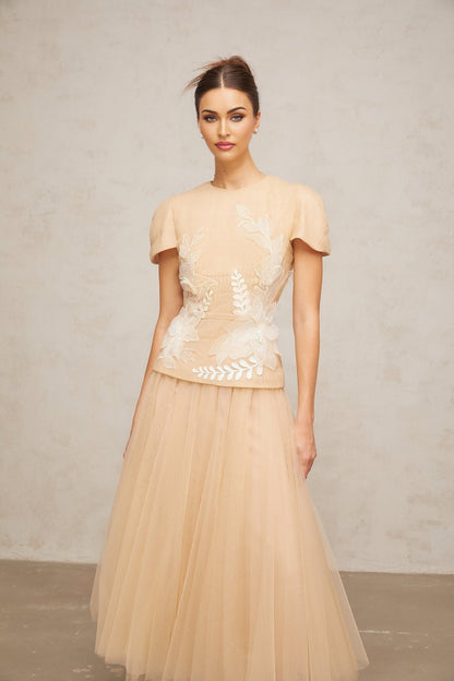 A matching set consisting of a top and skirt in white tulle fabric adorned with colorful floral appliqués The top features a sleeveless design while the skirt has a flowing silhouette Both pieces are decorated with delicate flower embellishments creating a romantic and feminine look