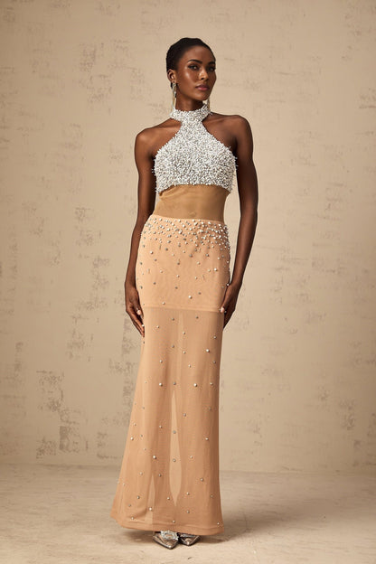 A long flowy white maxi dress with sheer elements adorned with small faux pearl embellishments throughout