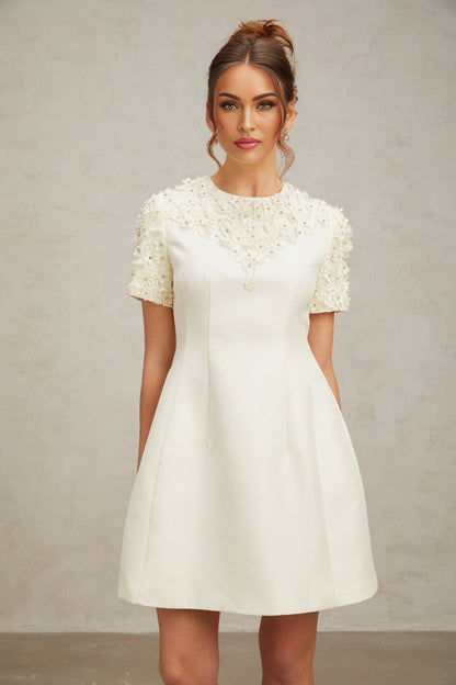 A short white mini dress with colorful floral applique designs scattered across the fabric featuring a fitted bodice and flared skirt