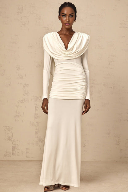 A woman wearing a long white fitted maxi dress with ruched detailing standing against a plain background