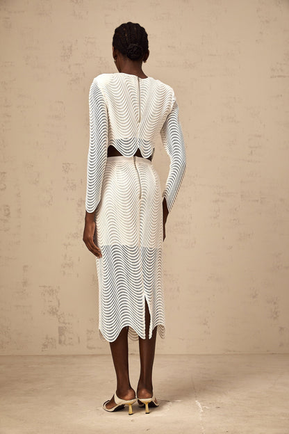 Woman wearing white matching set with wavy woven texture top and skirt standing against plain background