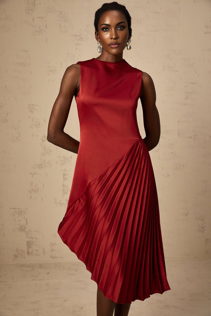 A woman wearing a wine red midi dress with an asymmetric neckline and pleated skirt standing in a neutral setting
