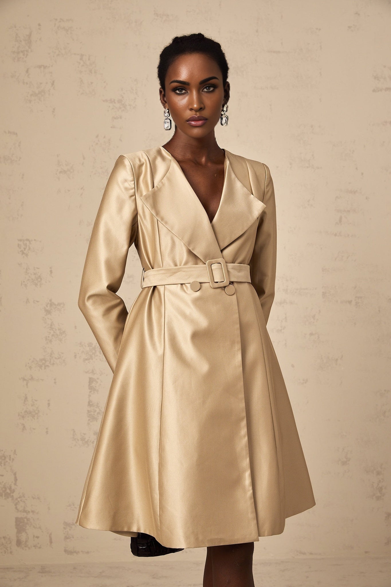 Woman wearing long khaki coat with belt cinched at waist