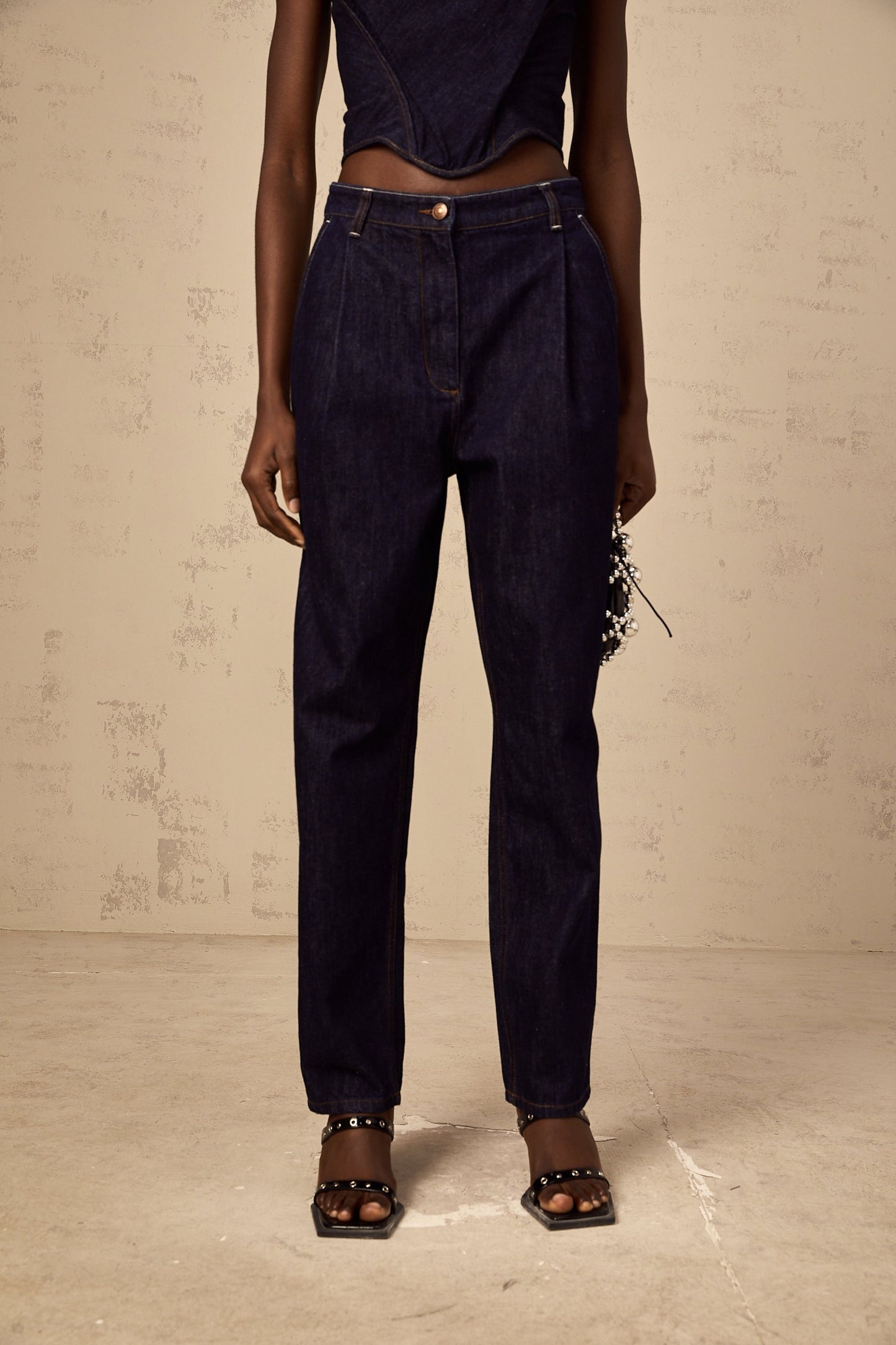 A pair of blue high rise jeans with pleated details on the front named Danae