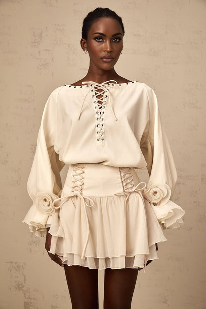 Woman wearing a matching blouse and skirt set in light fabric The blouse has ruffles and a self tie detail The skirt is flowy and coordinated with the top