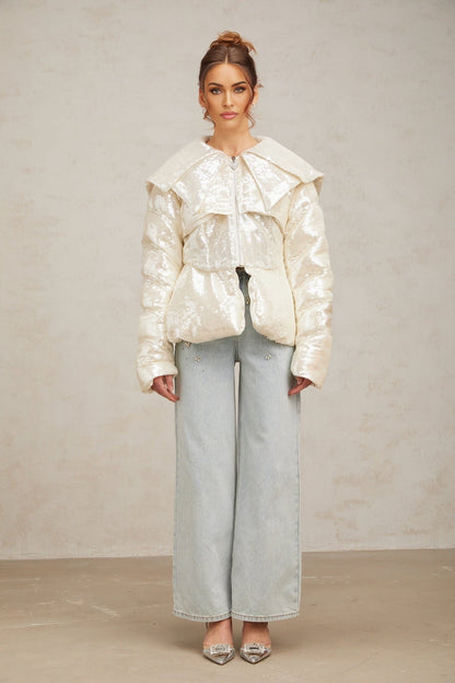 A white winter coat with sequin embellishments and down insulation featuring a woman named Joslyn wearing the garment