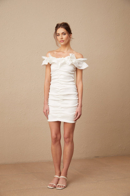 Young woman wearing white offshoulder ruffled mini dress standing against plain background