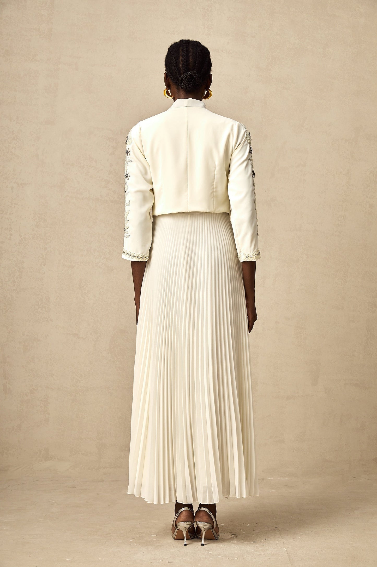 A white matching set featuring a pleated jacket and dress with embellished details The jacket has a structured silhouette while the dress is fitted Both pieces are adorned with delicate embellishments for an elegant look