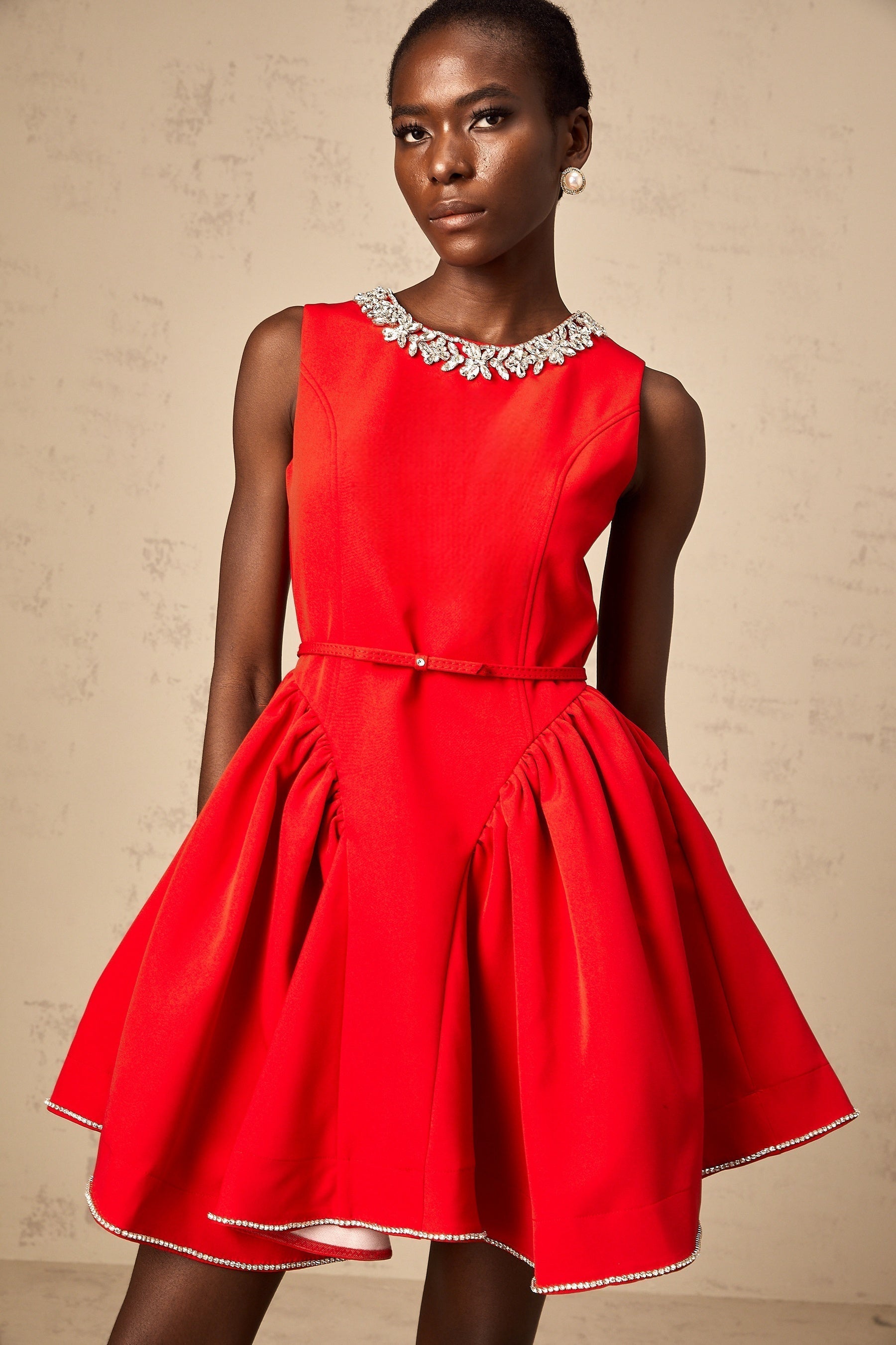 Woman wearing a short red dress with pleated skirt and embellished details