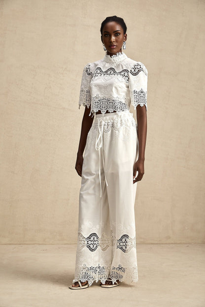 Woman wearing white lace trimmed cropped top and matching trousers set with cutout details