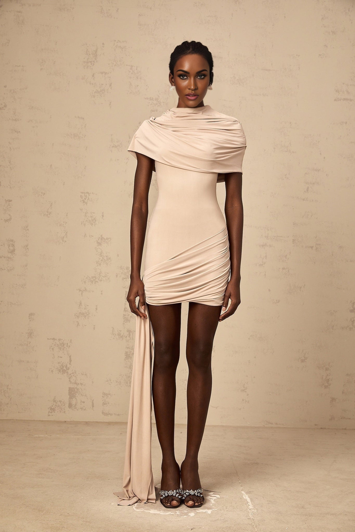 A woman wearing a lightcolored fitted mini dress with capelike sleeves and ruched detailing