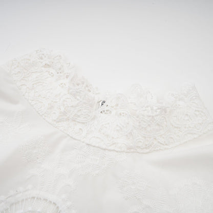 Woman wearing a matching set of white lace trimmed cropped top and trousers with cutout details