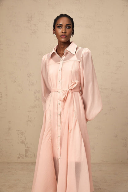 Woman wearing a pink midi length shirt dress with tied waist detail and button front closure