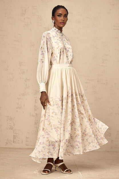 Woman wearing matching floral print shirt and skirt set Shirt has frilled details Skirt is midi length Set features wisteria pattern in blue and white tones