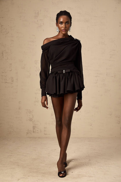A woman wearing a black asymmetric tulle blouse and matching skirt set The top features a one shoulder design with ruffled details The skirt is flowy and made of tulle fabric The outfit is elegant and suitable for formal occasions