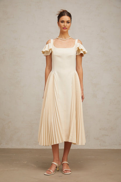 Woman wearing long beige pleated midi dress with flared skirt and neutral tones standing in relaxed pose