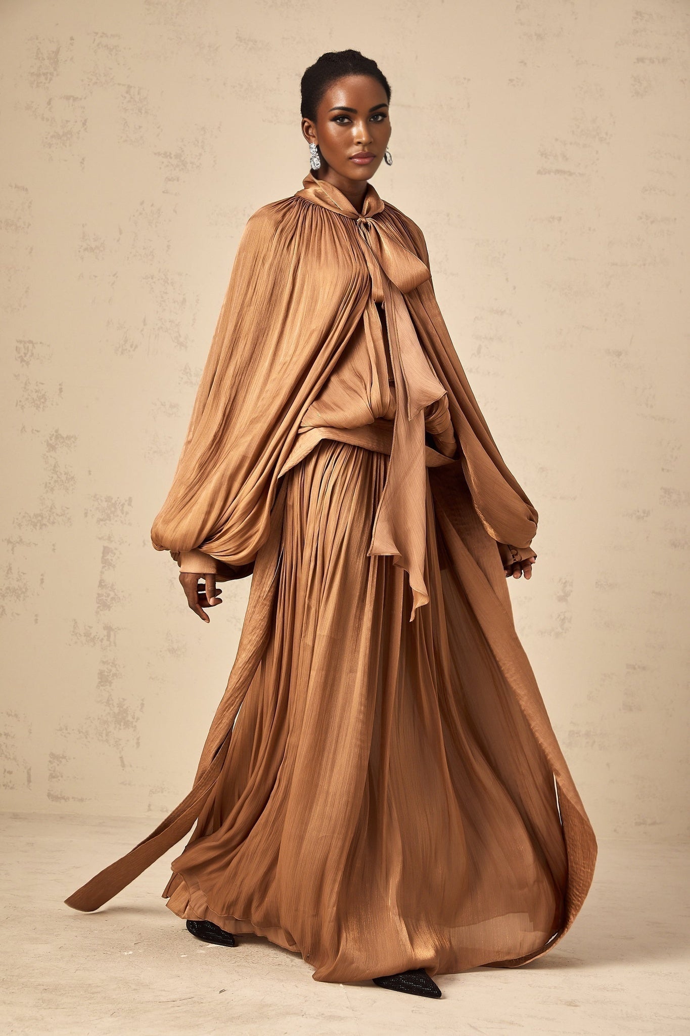 Woman wearing long brown pleated satin maxi dress with flowing skirt and fitted bodice