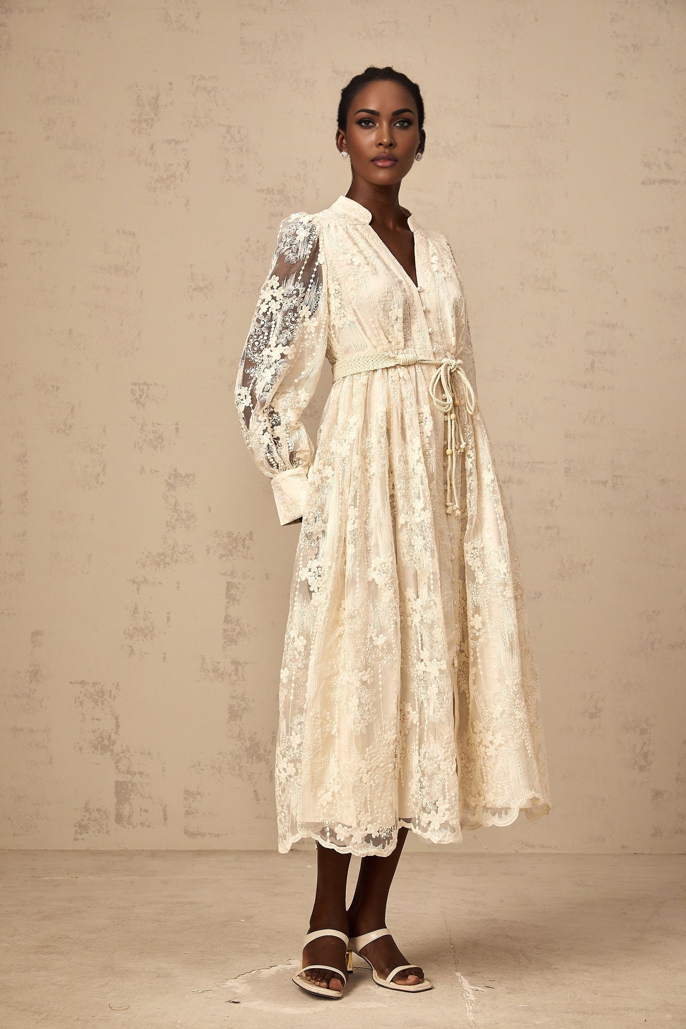 A woman wearing a neutralcolored midi dress with lace embroidery details standing in a relaxed pose